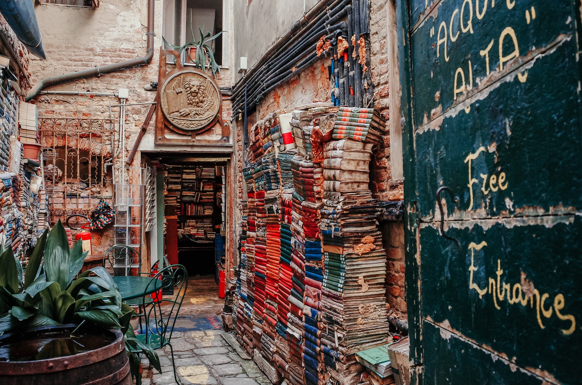 A vibrant old world back alley entrance to a overflowing bookstore with a bronze plaque over the door depicting a lion with a tablet.
